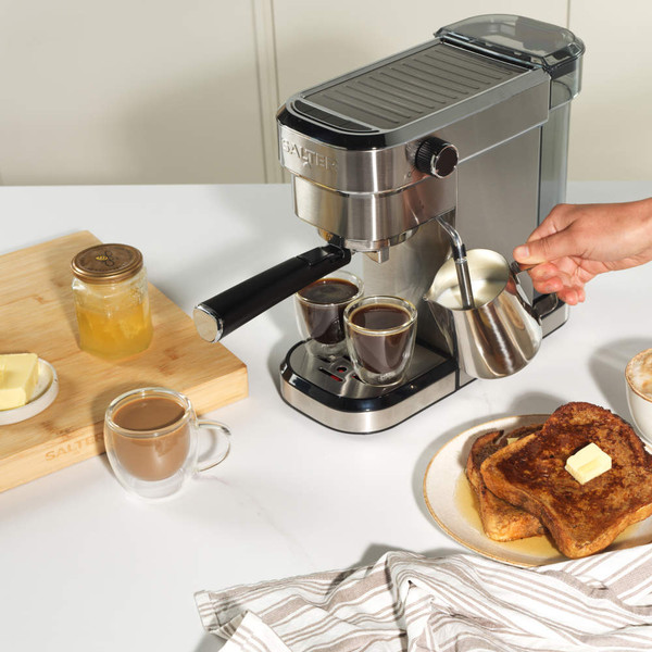 Silver espresso machine with cup of coffee, cappuccino mug, milk jug and filter