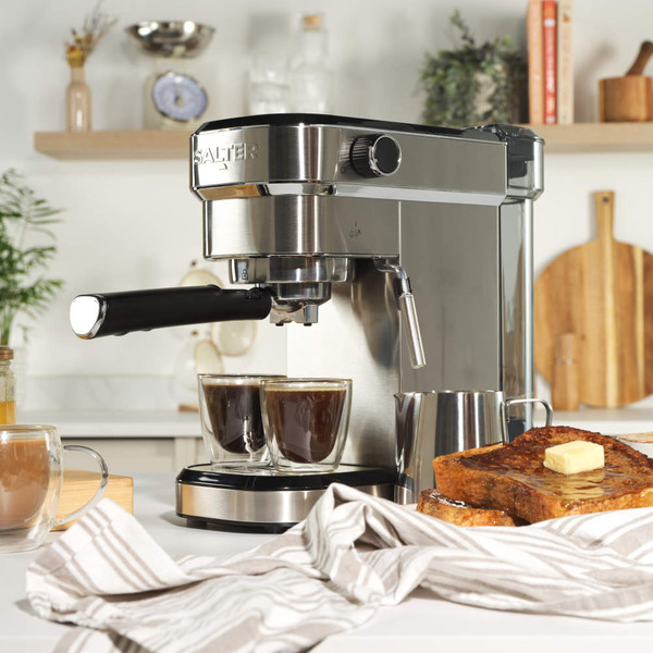 Silver espresso machine with cup of coffee, cappuccino mug, milk jug and filter