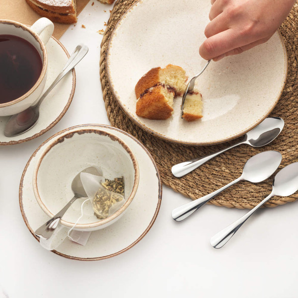 Table setting with cake, tea, ceramic crockery and stainless steel teaspoons.