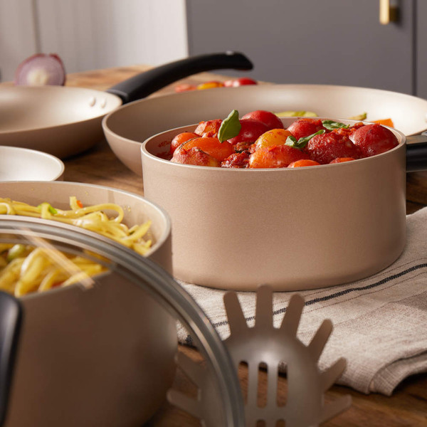Set of gold non-stick pans with tomato sauce and pasta, shown on a wooden kitchen surface