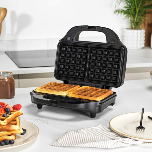 Black waffle maker open with two cooked waffles on kitchen counter