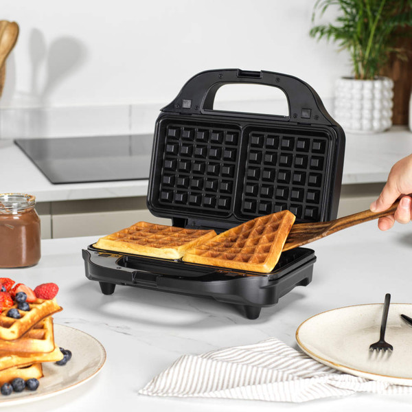 Black waffle maker open on kitchen counter with cooked golden waffles inside.