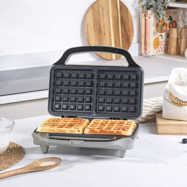 Electric waffle maker with two golden waffles, open on kitchen counter