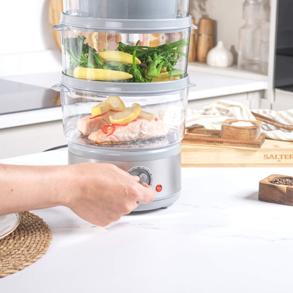 Electric food steamer with salmon and vegetables, dial being turned by hand