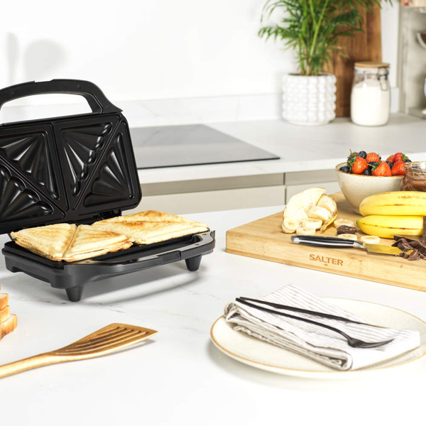 Black sandwich toaster with toasted sandwiches, shown in a kitchen setting.