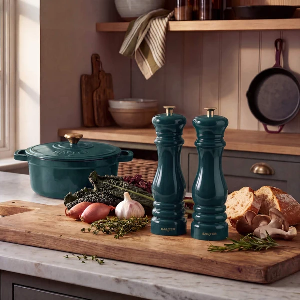 Green ceramic salt and pepper mills on kitchen counter with bread and vegetables