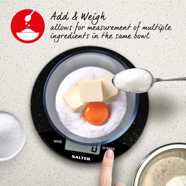 Glass bowl with milk being poured, shown on a black Salter digital kitchen scale.