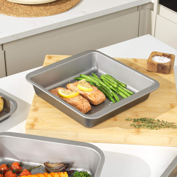 Grey square roasting tin with salmon fillets and green beans, shown on kitchen worktop