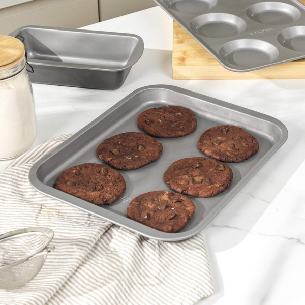 Non-stick baking tray with six chocolate cookies in kitchen setting