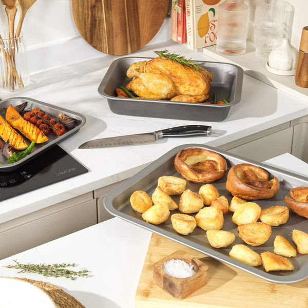 Grey non-stick roasting tray with baked butternut squash, tomatoes, and broccoli on kitchen counter