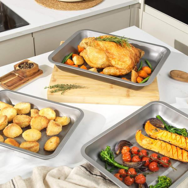 Set of three non-stick oven trays with roast chicken, potatoes, and vegetables