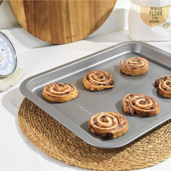 Non-stick grey bakeware set with roast chicken, vegetables, Yorkshires and cookies displayed.