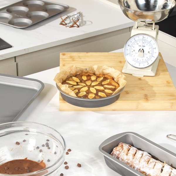 Round non-stick cake pan with baked apple cake on kitchen counter, baking accessories nearby
