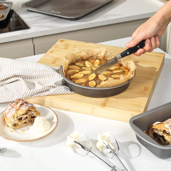 Round non-stick cake pan with baked apple cake on kitchen counter, baking accessories nearby