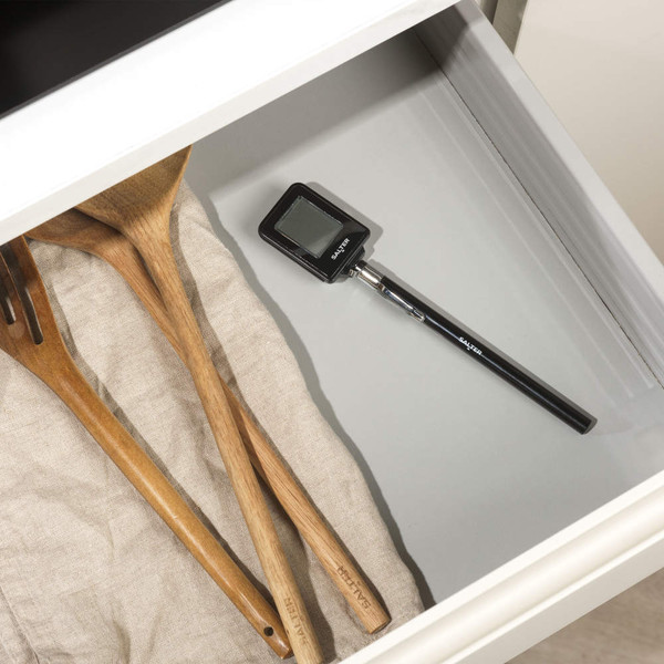 Digital cooking thermometer with black handle in kitchen drawer next to wooden utensils