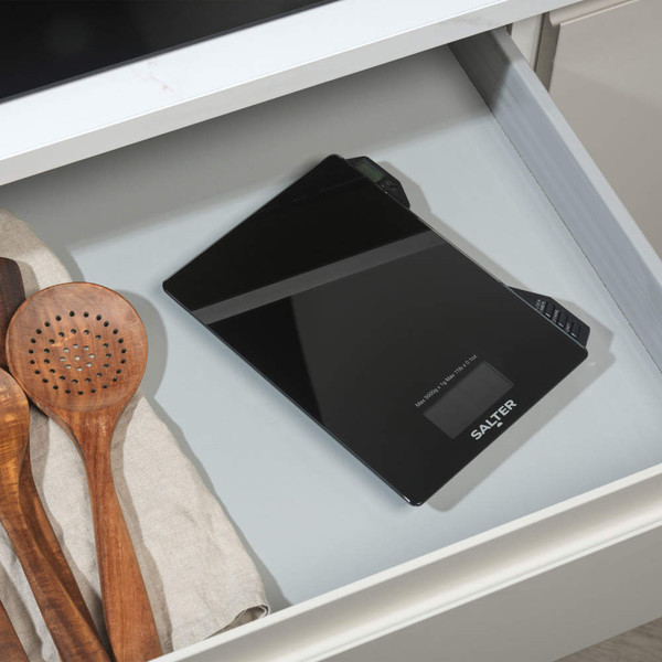 Black digital kitchen scale shown in a drawer with wooden utensils.
