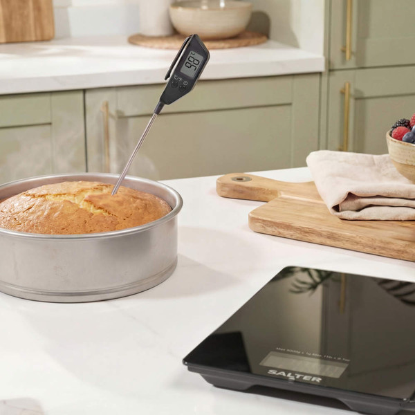 Digital kitchen thermometer in cake, black Salter kitchen scale on counter