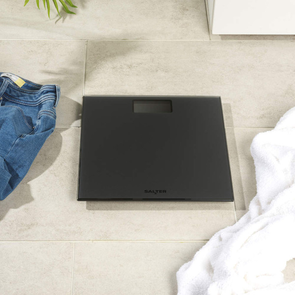 Black digital bathroom scale on tiled floor, shown from above.