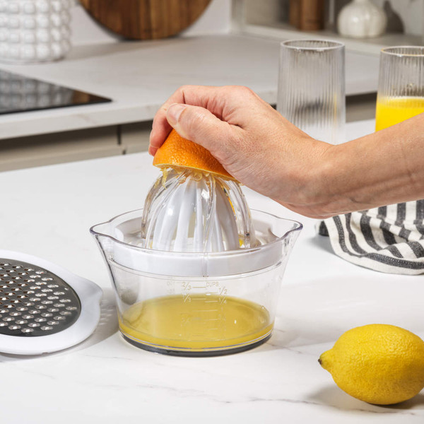 Manual citrus juicer in use, clear container with white reamer, fresh lemons on worktop