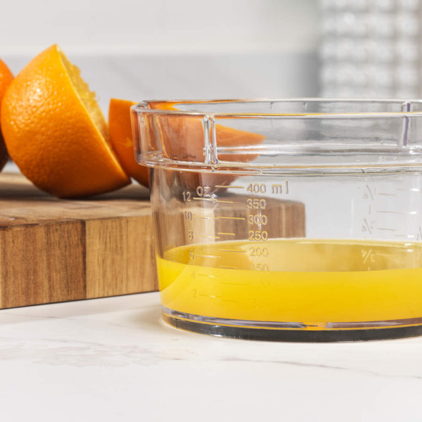 Glass measuring jug with fresh orange juice and sliced oranges on wooden board