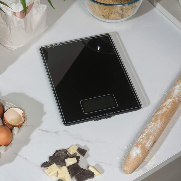 Black glass digital kitchen scale on a worktop with baking ingredients