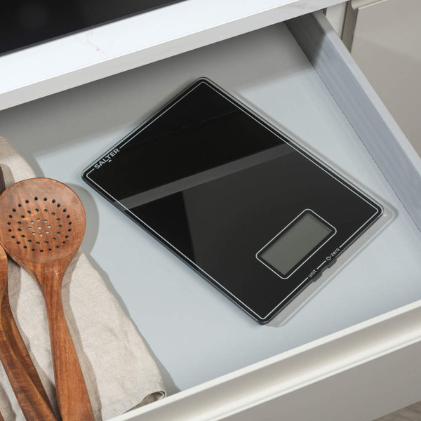 Black glass digital kitchen scale in drawer next to wooden utensils