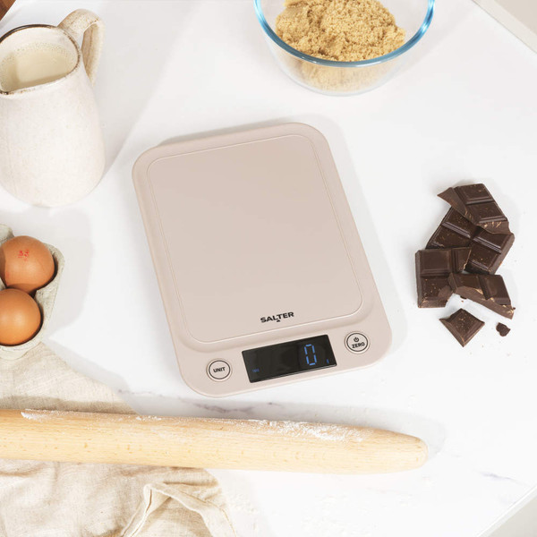 Digital kitchen scale in cream, shown with eggs, chocolate, flour and baking ingredients