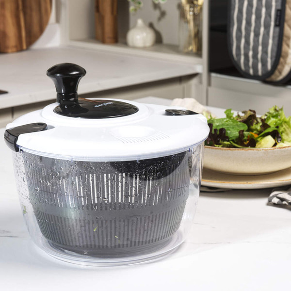 Salad spinner with black and white lid, shown on kitchen counter near fresh salad