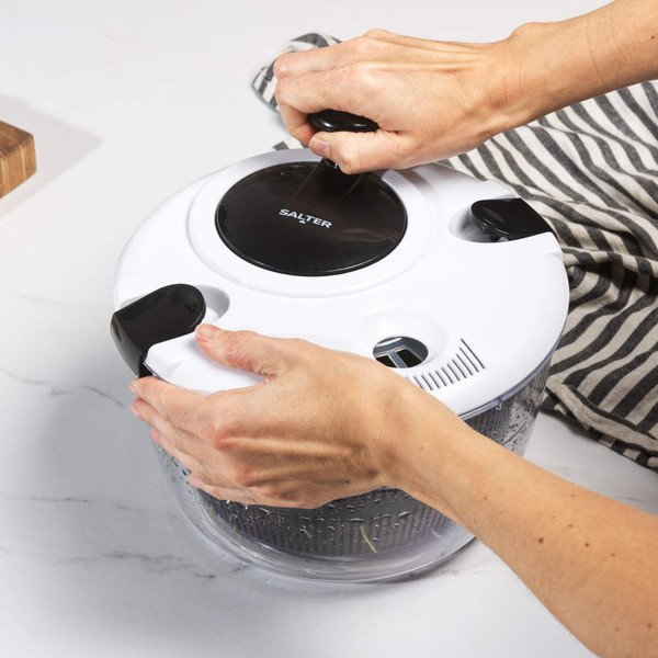 White salad spinner with black details shown in use on a kitchen worktop.