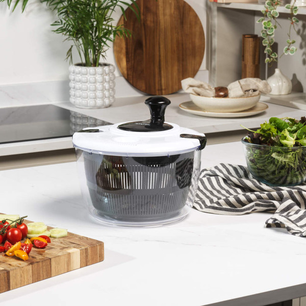 Clear plastic salad spinner with black handle on kitchen counter