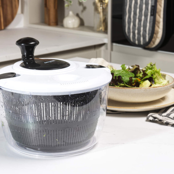 Salad spinner with black and white lid, shown on kitchen counter near fresh salad