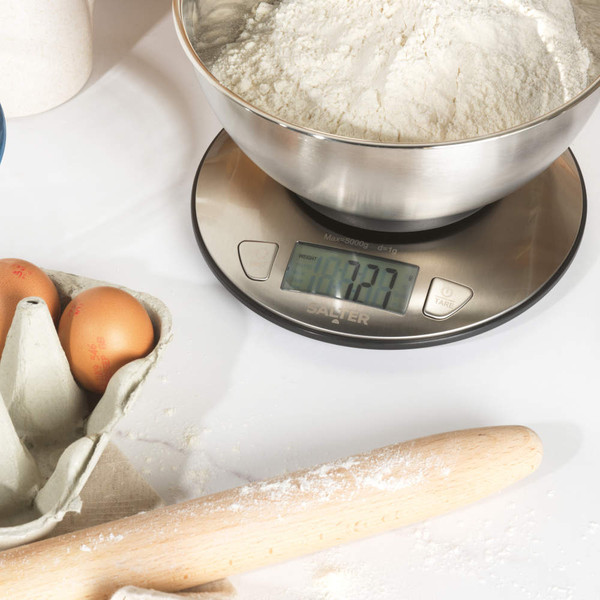 Digital kitchen scale in use with a bowl of flour on top, on a kitchen counter