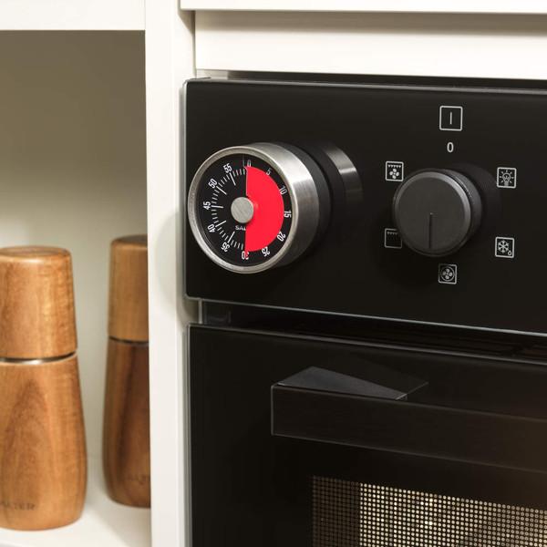 Kitchen timer with red dial attached to oven control panel, shown in use.