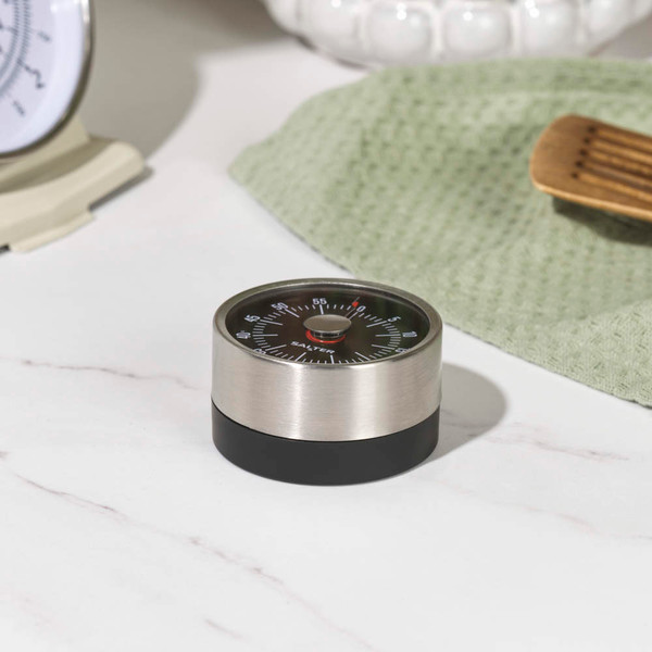 Silver mechanical kitchen timer with black base, being set by hand