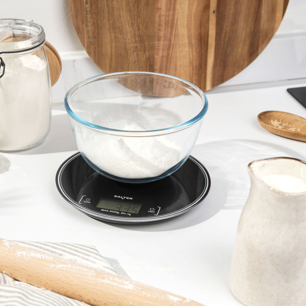 Digital kitchen scale with dark chocolate pieces on top, black glass surface, baking context