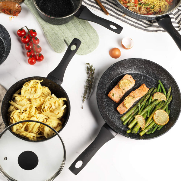 Non-stick black frying pans with cooked salmon, green beans, lemon slices and tagliatelle pasta.