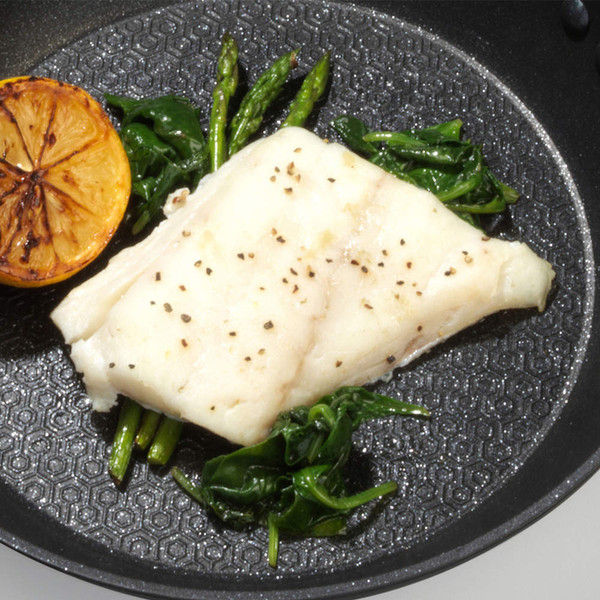 Cooked white fish fillet with grilled lemon, asparagus and spinach in frying pan