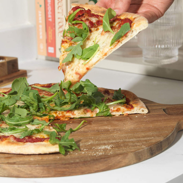 Thin crust cheese pizza topped with fresh rocket leaves, one slice being served.