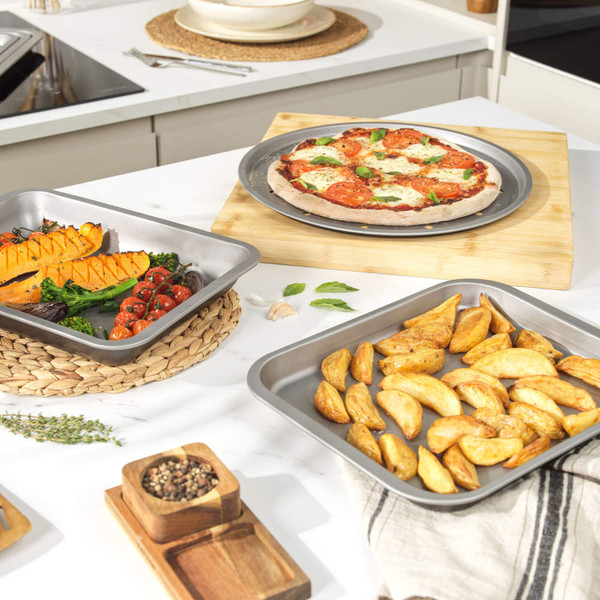 Assorted non-stick baking trays shown with roast chicken, Yorkshire puddings, cookies and potato wedges