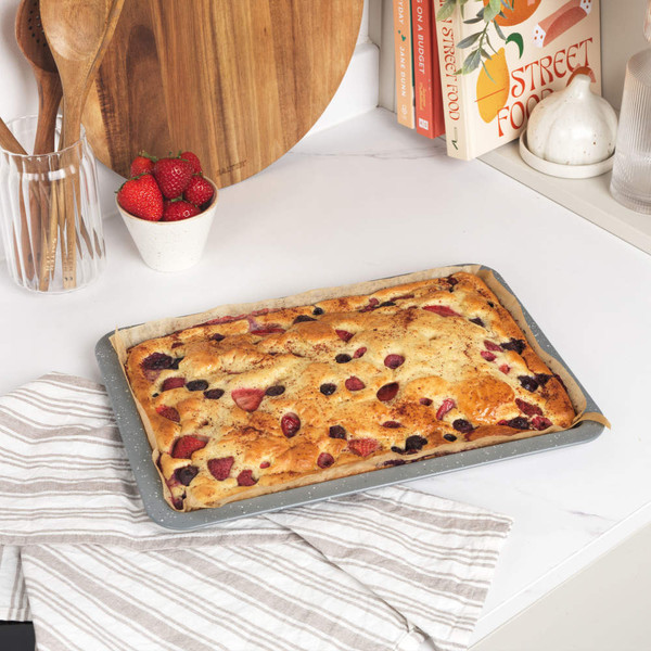 Tray-baked strawberry and mixed berry cake on striped tea towel, kitchen worktop