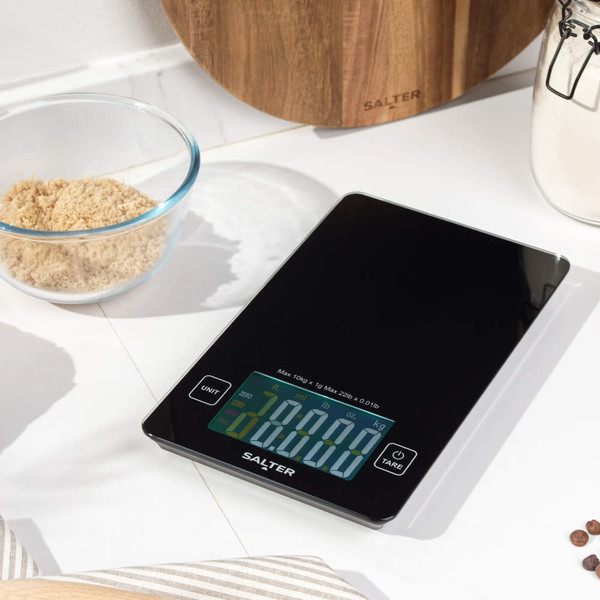 Black digital kitchen scale with touchscreen display on worktop, shown in kitchen setting