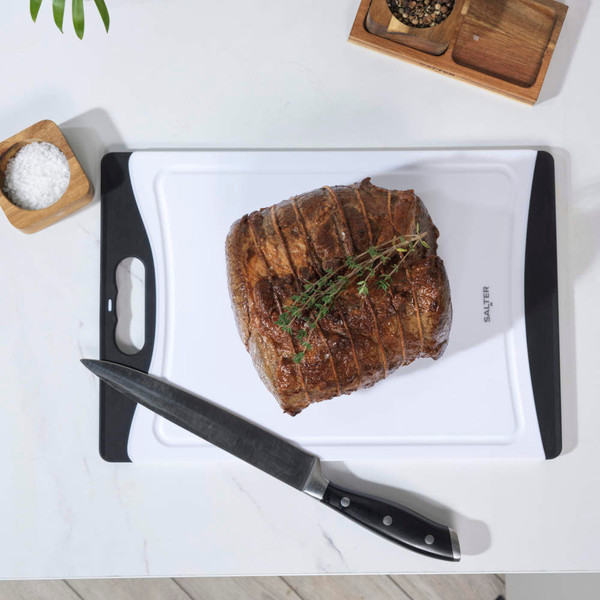 White chopping board with black edges, chef’s knife, sliced carrot and red onion.