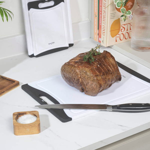 White chopping boards with knives, roast joint, and citrus fruit on modern kitchen counter