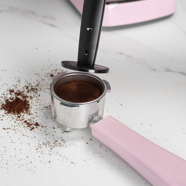 Portafilter with pink handle filled with ground coffee on white surface, for espresso machine