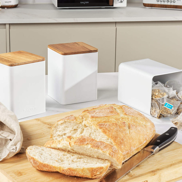 Set of white kitchen storage tins with wooden lids and a loaf of bread on board