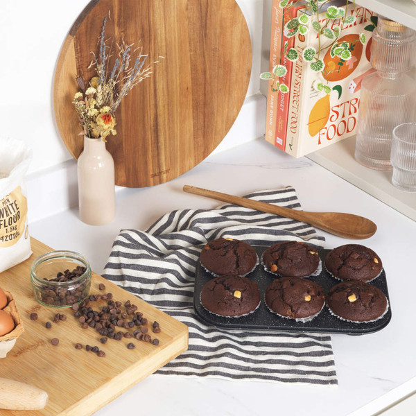 Tray of six chocolate muffins with white chocolate chips on striped tea towel in kitchen
