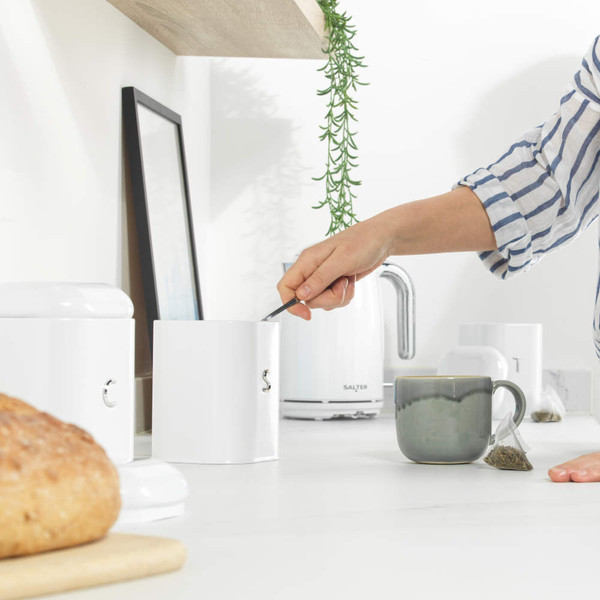 Kitchen scene with hand taking tea from white canister, next to mug and fresh bread