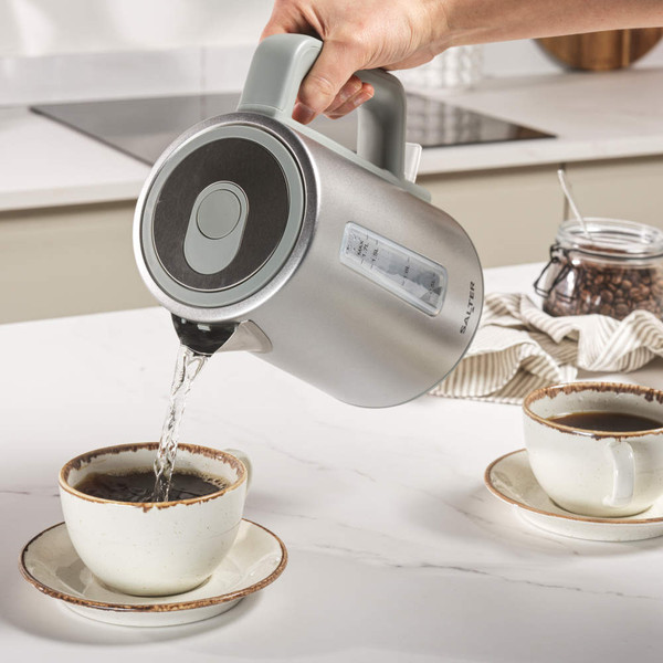 Grey handled electric kettle pouring hot water into a dark mug, product in use
