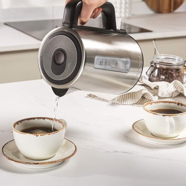 Stainless steel electric kettle pouring hot water into cup on kitchen counter