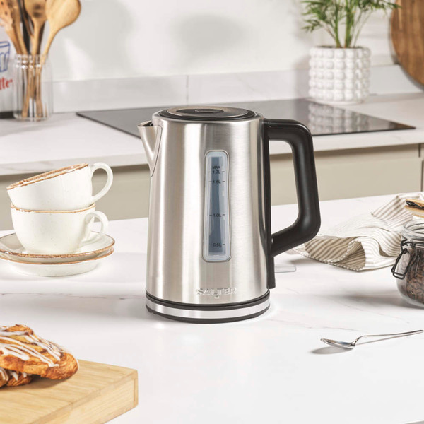Stainless steel electric kettle with black handle, being switched on by a person's finger